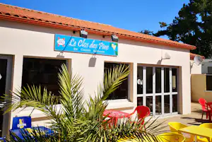 Campinghaus mit rotem Ziegeldach, Terrasse mit gelben Stühlen und roten Liegestühlen sowie Beschilderung am Eingang.