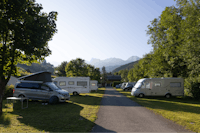 Campasun Camping Le Clos du Pin - Standplätze mit Wohnwagen und Wohnmobilen in der Abendsonne umgeben von Bäumen mit Blick auf die Berge