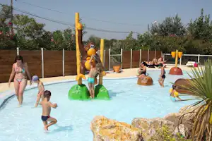 Kinder spielen im Schwimmbecken eines Campingplatzes, mit Wasserspielzeug und bunten Schwimmhilfen am Beckenrand.