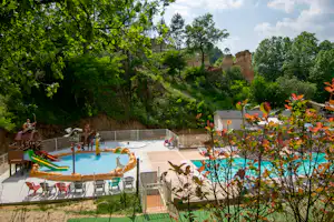 Schwimmbecken auf einer Campinganlage mit Liegestühlen, Treppe und Blick auf Bäume und einen bewaldeten Hang.