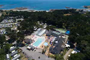 Luftaufnahme einer Campinganlage mit Schwimmbecken, vielen Mobilheimen und Bungalows im Grünen, dahinter das Meer.