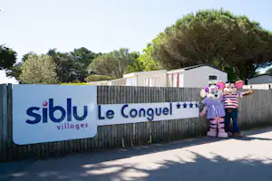 Eingangsschild „Siblu Le Conquel“ am Campingplatz, dahinter Mobilheime und Bäume, im Vordergrund zwei Figuren.