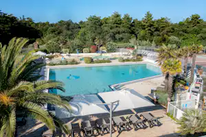 Großer Camping-Pool mit türkisfarbenem Wasser, Liegen und Sonnenschirmen, Palmen und gepflegten Wegen im Hintergrund.