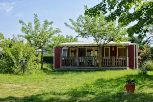 Bungalow mit Terrasse und Markise auf einem Campingplatz, umgeben von Bäumen und gepflegtem Rasen.