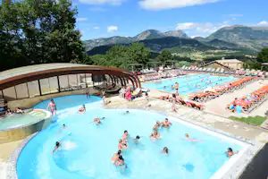 Großes Camping-Schwimmbad mit mehreren Becken, Liegen und Blick auf grüne Berge und einen See in der Ferne.