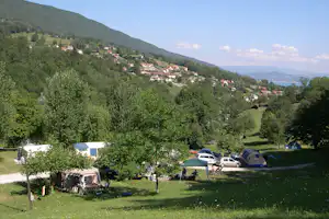 Campingplatz mit Zelten und Autos am Hang, Blick auf ein Dorf im Tal und den See in der Ferne.