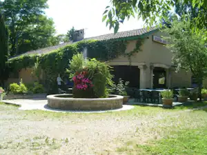 Rundes Steingewächsbeet vor einem Campinghaus mit Terrasse, Tischen und Stühlen im Garten mit Hecken und Bäumen.