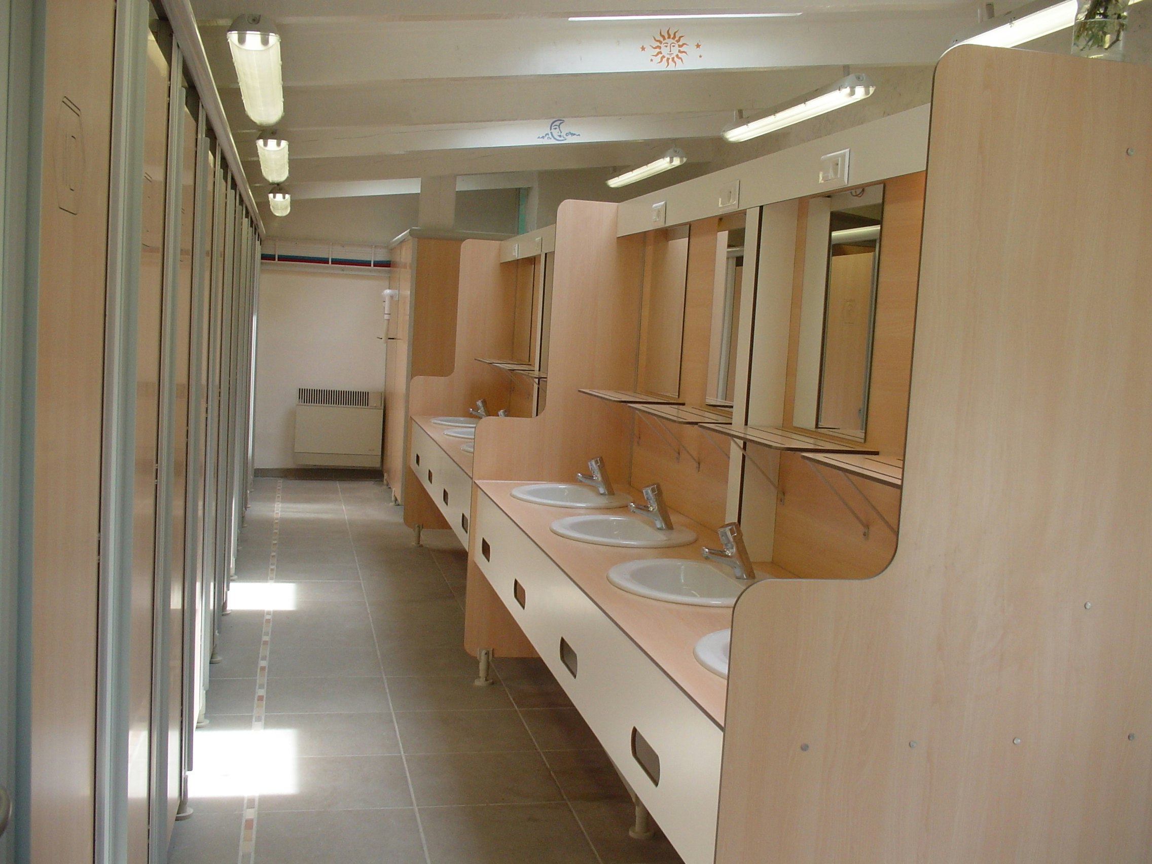 Reihe von Waschbecken in einem hellen Sanitärraum im Campingbereich, mit langen Flurwänden und Deckenleuchten.