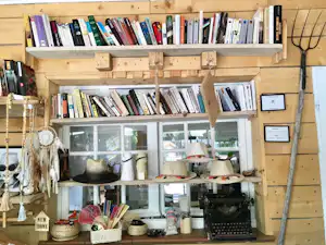 Bücherregal in einer Camping-Lounge mit vielen Büchern, Deko, Schreibmaschine und Regalen an einer Holzverkleidung.