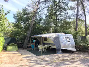 Wohnwagen und Zelt auf einem Stellplatz im Grünen, mit Tisch und Stühlen vor dem Wohnwagen zwischen Bäumen.