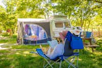 Camping Le Domaine d' Anglas - Camper liest ein Buch im Liegestuhl auf dem grünen Stellplatz für Zelte und Wohnwagen