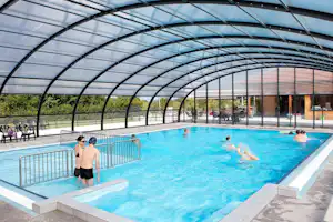 Überdachtes Schwimmbecken mit Treppenstufen, Absperrgittern und mehreren Schwimmern im blauen Wasser.