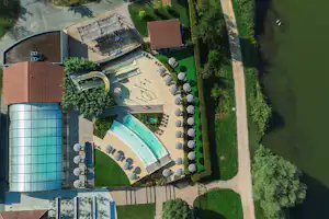 Luftaufnahme eines Campingplatzes mit Schwimmbecken, Sonnendeck, Liegen und Beckenbereich neben einem großen Gebäude und Wegen.
