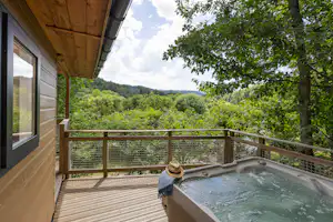 Whirlpool auf der Camping-Terrasse mit Blick in den grünen Wald, Holzgeländer und Hauswand im Vordergrund.
