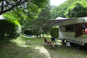 Wohnmobil mit Markise auf dem Campingplatz, Campingstühle und Tisch im Schatten der Bäume, Wiese und Wege im Hintergrund.