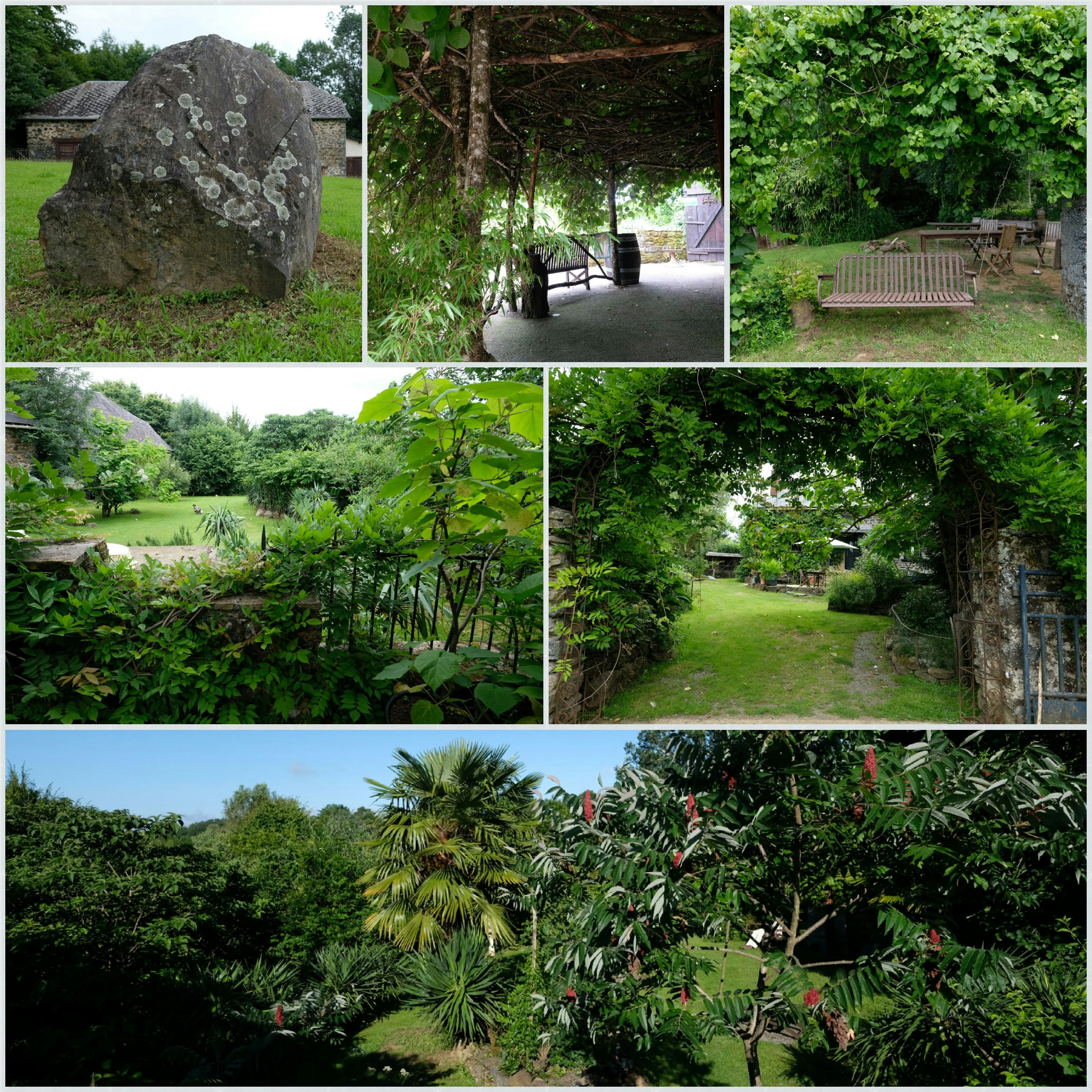 Campinggarten mit viel Grün, Bäumen und Wegen; im Hintergrund ein großer Felsbrocken und Sitzgelegenheiten im Schatten.