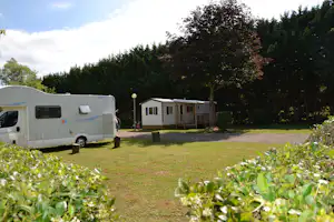 Wohnmobil auf einem Campingplatz-Stellplatz, Rasenfläche und Hecken, im Hintergrund mobile Unterkünfte und Bäume.