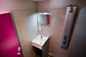 Waschbecken mit Spiegel im Camping-Badezimmer, geflieste Wände, Handtuchhalter und Spender an der Wand.