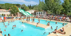 Großes Camping-Schwimmbecken mit vielen Badegästen, Liegen und Sonnenschirmen, im Hintergrund Bäume und Gebäude.