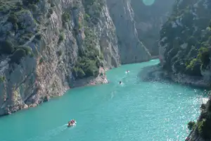 Türkisfarbener Fluss in einer engen Schlucht, umgeben von steilen Felswänden und dichtem Grün, mit Booten im Wasser.