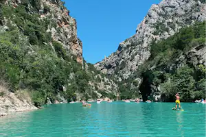 Türkisfarbenes Wasser in einer Bergschlucht, links und rechts Felswände, im Vordergrund ein Stand-Up-Paddler.
