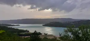 Weite Aussicht auf eine Bucht mit ruhigem Wasser, Uferlinie und bewaldeten Hügeln in der Ferne.