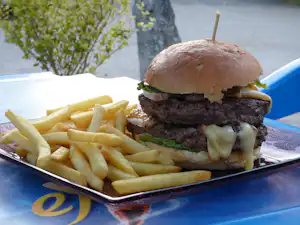 Burger mit Rindfleisch und Käse auf einem Tablett, daneben Pommes auf blauem Camping-Tisch.