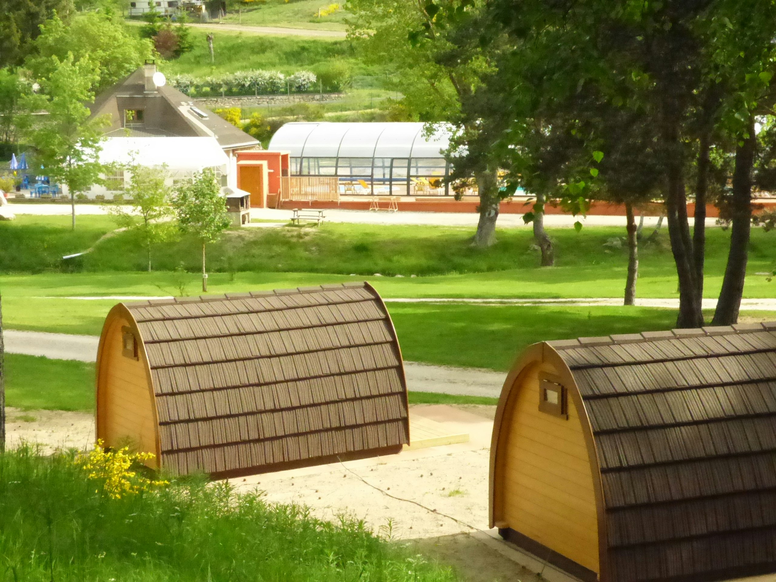 Zwei Campingzelte mit braunen Wänden stehen auf einem Kiesweg im grünen Garten, im Hintergrund Gebäude und Bäume.