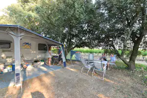Campingstellplatz mit Zeltvorzelt, Sitzgruppe und Stühlen unter Bäumen, daneben weitere Zelte und ein Tisch.