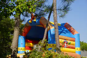 Aufblasbares Kinderzelt mit bunten Motiven zwischen Kiefern, im Vordergrund Äste und Baumstämme.