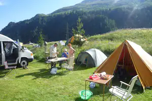 Campingzelt auf einer grünen Wiese, daneben Wohnmobil und Picknicktisch, im Hintergrund Berge und Nadelwald.