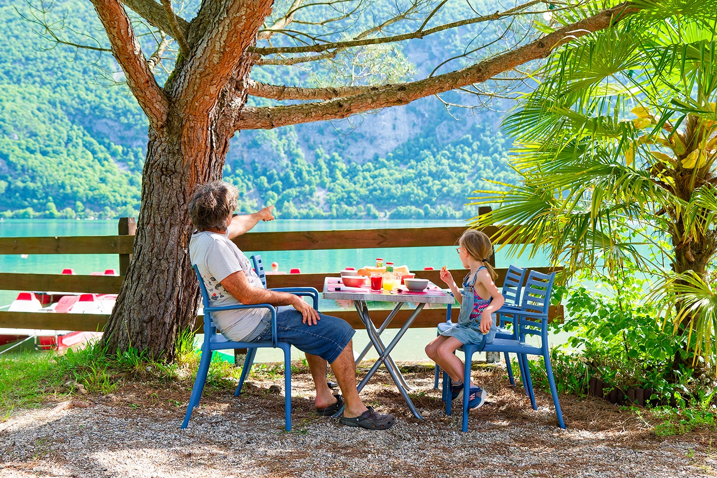 Camping Le Hameau Des Pêcheurs - Camper und Kind essen gemeinsam an einem Tisch am Ufer des Sees