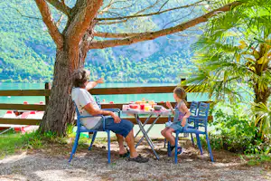 Camping Le Hameau Des Pêcheurs - Camper und Kind essen gemeinsam an einem Tisch am Ufer des Sees