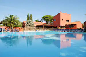 Schwimmbad mit blauem Wasser, Reihe von Sonnenliegen und einem roten Gebäude mit Terrasse und Geländer.