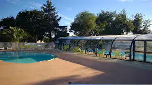 Beheizter Poolbereich mit Sonnenliegen und Überdachung am Campingplatz, umgeben von Bäumen und Hecken.