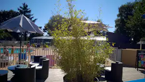 Holzterrasse mit Sitzgelegenheiten und Sichtschutz, im Hintergrund Zelte und ein Poolbereich mit Liegen.