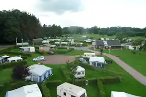 Campingplatz mit Wohnwagen und Zelten, gepflasterten Wegen und Rasenflächen zwischen Hecken und Bäumen.