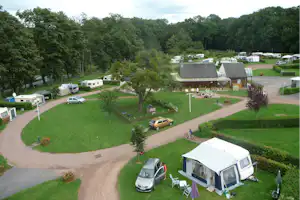 Campingplatz mit Wohnmobilen, Zelten und Autos auf gepflegenen Stellplätzen, umgeben von Bäumen und Rasenflächen.