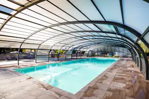 Überdachtes Schwimmbecken mit klarem Wasser, Stegen aus Holz und Glaswänden im Campingbereich.