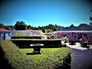 Campinganlage mit Terrasse, Sitzbereich und Grill im Garten, daneben mehrere Mobilheime und viel Grün vor blauem Himmel.