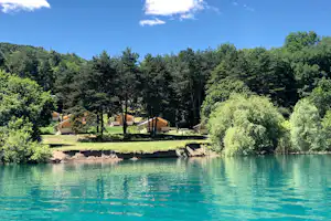 Campingplatz am See mit mehreren Zeltunterkünften zwischen Bäumen, Rasenfläche und Uferlinie im Hintergrund.