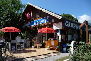Camping-Rezeption in einem Holzgebäude mit Schildern, roten Marktschirmen und Fahrrad vor dem Eingangsbereich.