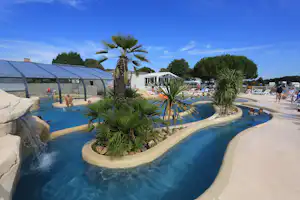 Poolanlage mit Palmen, Wasserrutsche und Sonnenschirmen, daneben ein überdachter Bereich und weitere Gäste am Campingplatz.