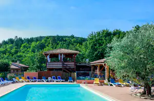 Pool am Campingplatz mit Liegestühlen, Holzüberdachung und Blick auf grüne Bäume und Hügel im Hintergrund.