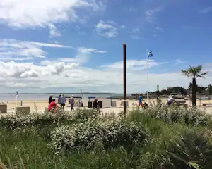Weg im Campingbereich mit Blumenbeeten, Fahrrädern und Blick auf das Meer und eine Mauer am Strand.