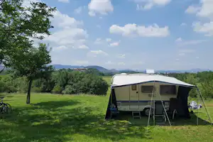 Wohnwagen-Zelt auf einer grünen Campingwiese, mit geöffnetem Vorzelt und Blick auf Bäume und Hügel in der Ferne.
