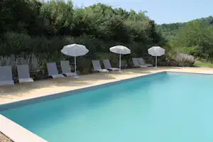 Schwimmbad auf der Terrasse mit mehreren Liegestühlen, Sonnenschirmen und Steinmauer im Grünen.