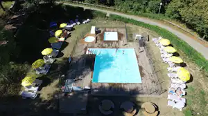 Großes Schwimmbecken auf einem Campingplatz mit Liegen, gelben Sonnenschirmen und Sitzbereichen, umgeben von Rasen und Wegen.