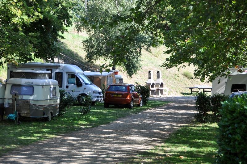 Wohnwagen und Auto auf einem Campingplatz, daneben ein weiterer Camper, schattiger Weg zwischen Bäumen.