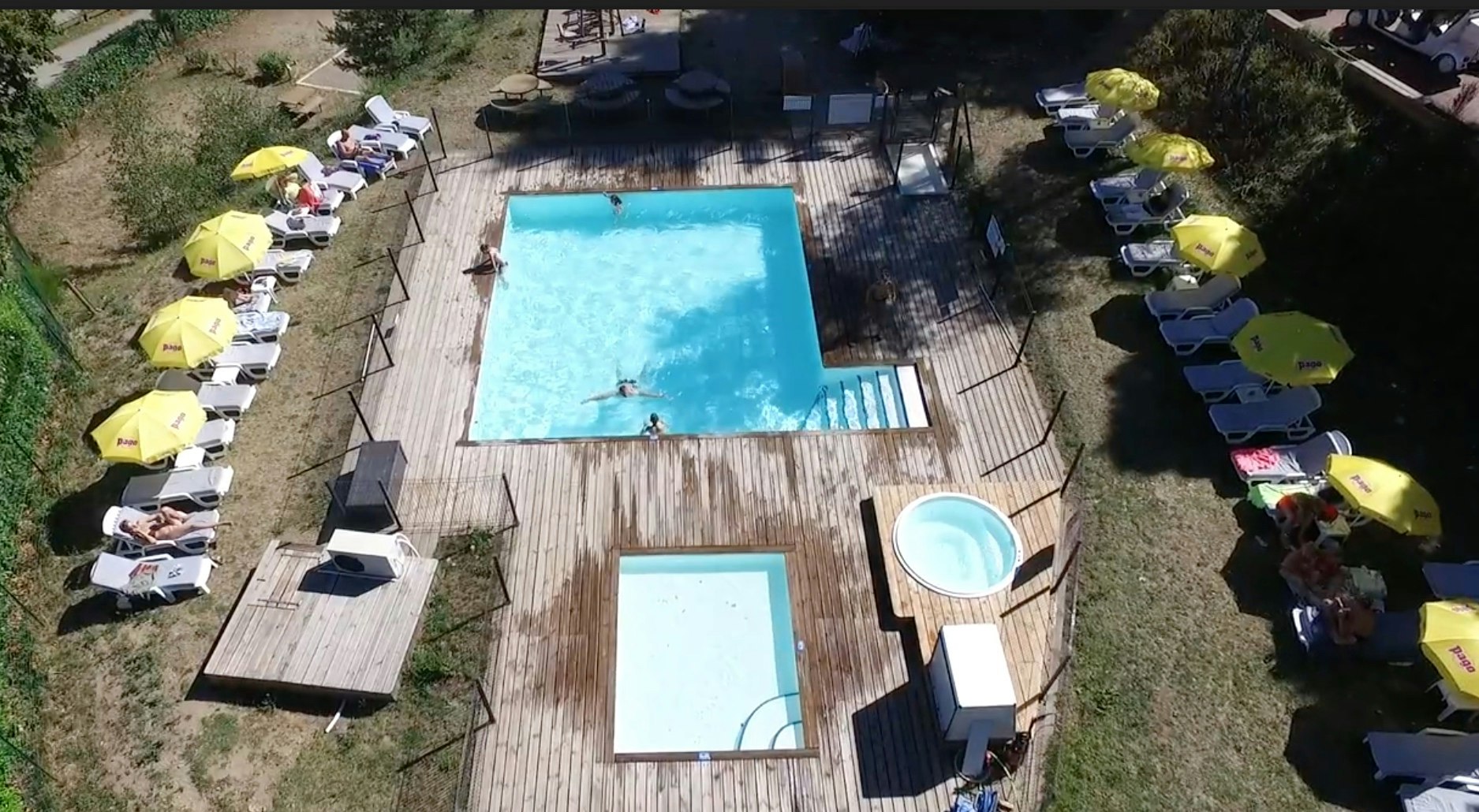 Großer Camping-Pool mit Liegen und Sonnenschirmen, daneben ein kleineres Becken, umgeben von Rasen und Wegen.